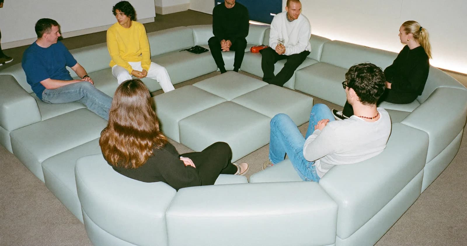 Zona de sillones bajos donde varias personas conversan sentadas, sin escenario ni presídium.