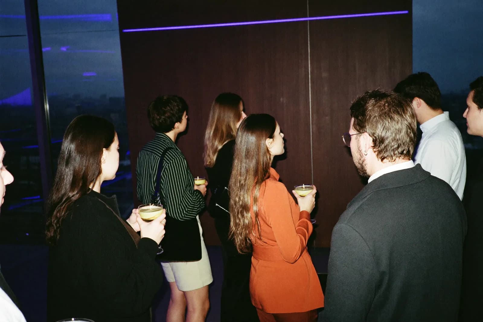 Cóctel de networking en interior, con tres asistentes conversando de pie con una copa en la mano.